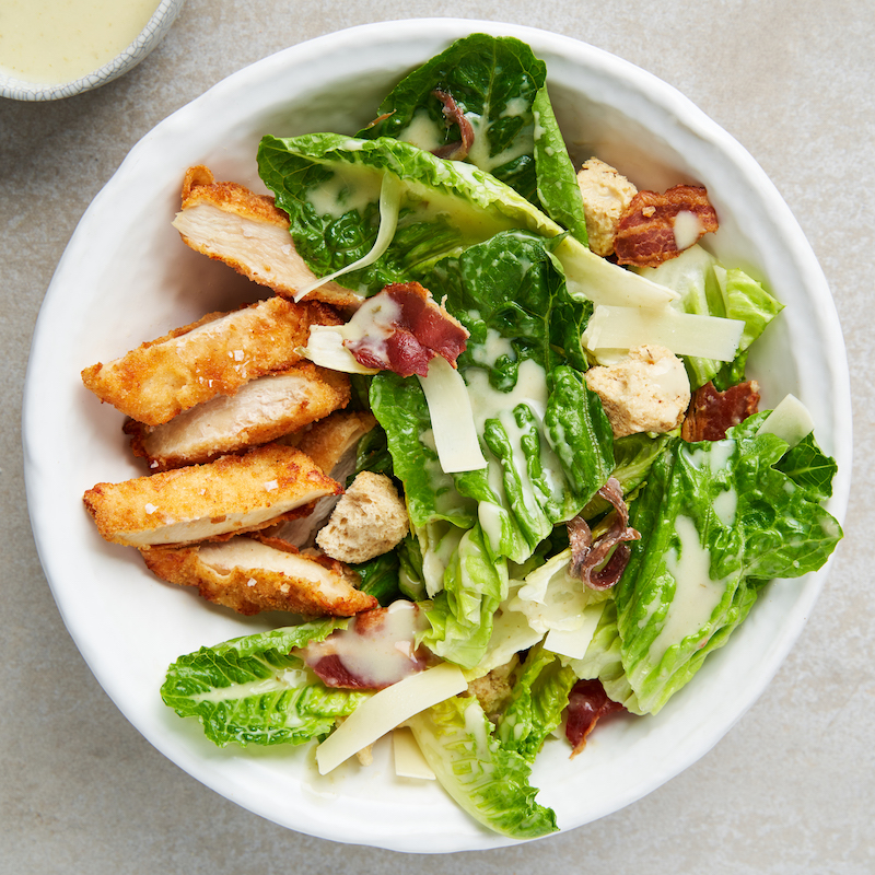 Bowl of Thai Basil & Coconut Chicken Caesar Salad in a white bowl, shot from above